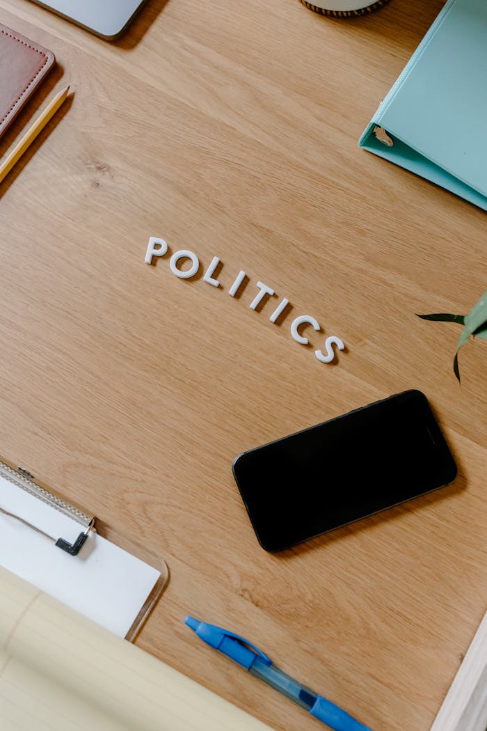 A modern office desk with a smartphone, notebooks, and 'politics' spelled out, showcasing a conceptual theme.